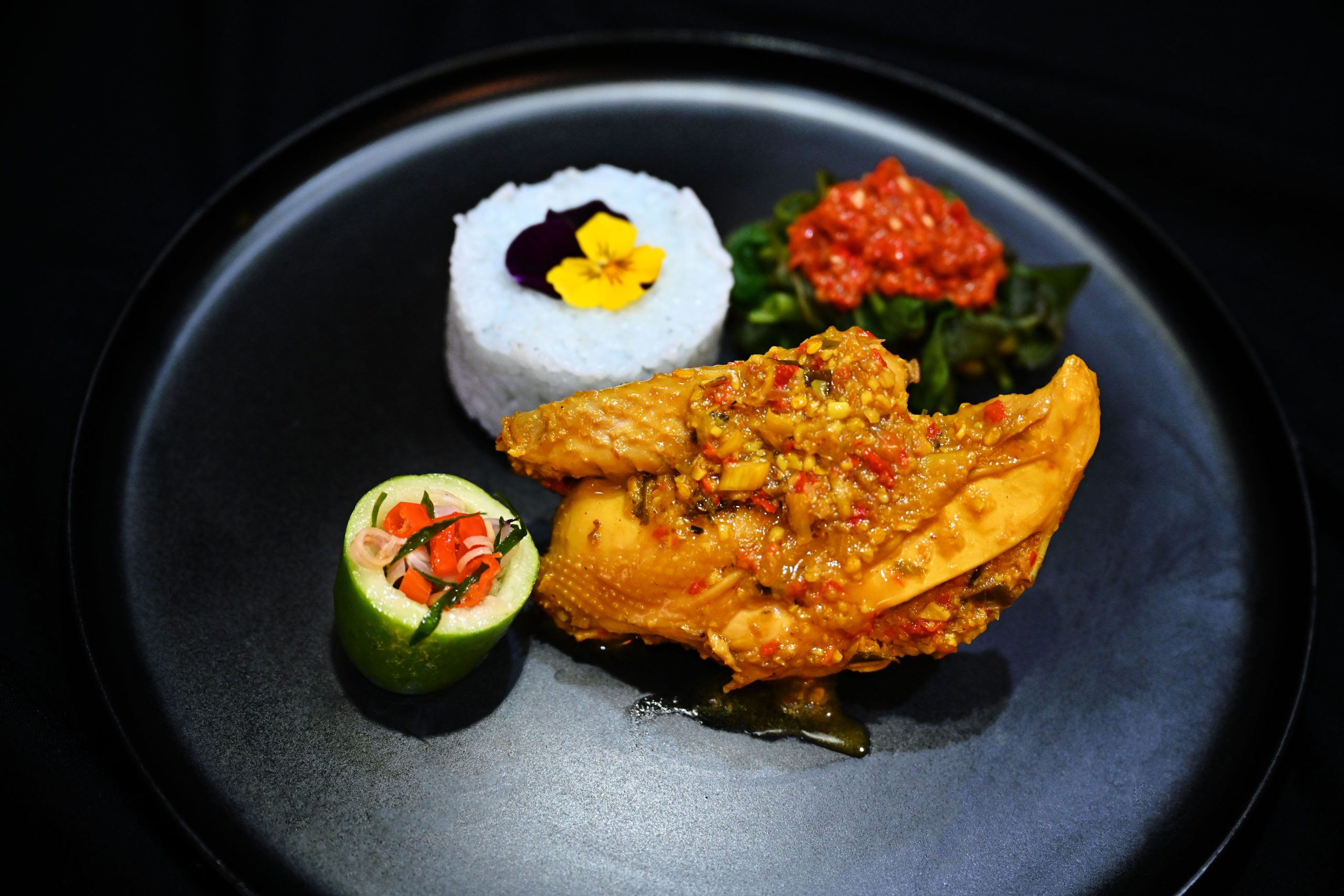 Balinese ayam betutu served with rice and vegetables on a plate.